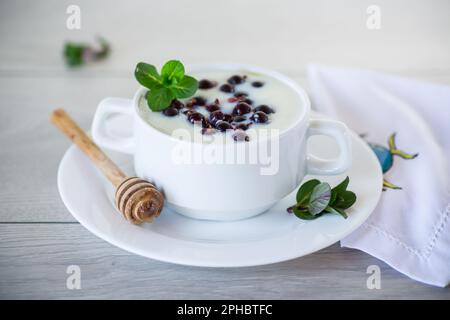 Gekochter Milch-Grieß-Haferbrei mit Beeren und Honig auf einem Teller, auf einem Holztisch. Stockfoto