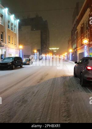 Nachts fällt Schnee auf einer schneebedeckten Straße der Stadt. Stockfoto