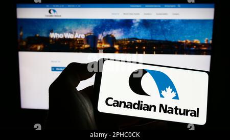 Person, die ein Smartphone mit dem Logo des Unternehmens Canadian Natural Resources Limited auf dem Bildschirm vor der Website hält. Konzentrieren Sie sich auf das Display des Telefons. Stockfoto