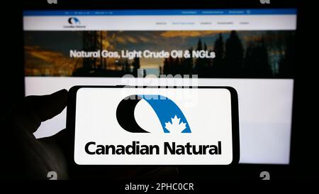 Person, die ein Mobiltelefon mit dem Logo des Unternehmens Canadian Natural Resources Limited auf dem Bildschirm vor der Unternehmenswebseite hält. Konzentrieren Sie sich auf das Display des Telefons. Stockfoto