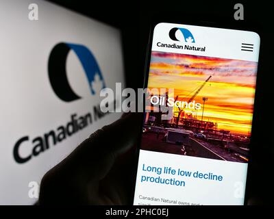 Person mit Smartphone und Webseite des Unternehmens Canadian Natural Resources Limited auf dem Bildschirm vor dem Logo. Konzentrieren Sie sich auf die Mitte des Telefondisplays. Stockfoto