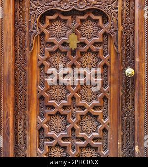 Alte Holztür, dekoriert mit orientalischen Ornamenten, typisch für Marokko, Metall hamsa - palmenförmiges Amulett - hängt oben Stockfoto