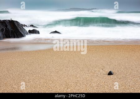 Wellenbrecher mit einsamen Felsen am Strand Stockfoto