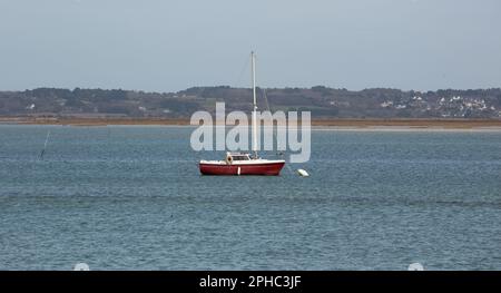 Ein rotes Segelboot ist in einer Bucht vor Anker, das Wasser bewegt sich nicht, die weiße Boje vor dem Laderaum ist an Ort und Stelle. Stockfoto