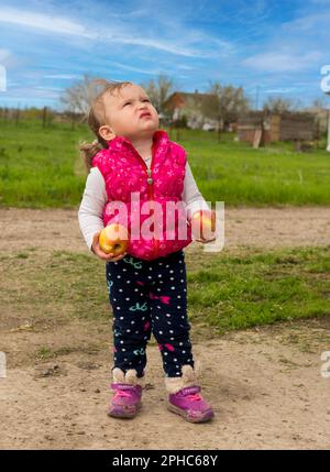 Das Mädchen steht auf der Straße und sieht hoch, hält Äpfel in der Hand Stockfoto