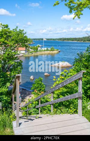 Sonniger Tag in einer kleinen Dorfbucht auf der Insel Vaxholm. Holztreppe hinunter zum kleinen Strand. Stockholmer Archipel, Schweden Stockfoto