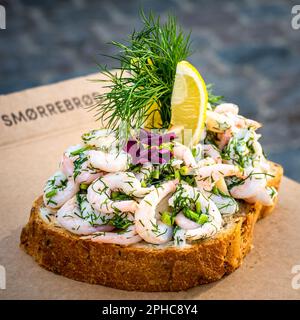 Traditioneller köstlicher dänischer Snack namens smørrebrød Butterbrot, reich geschmückt mit Garnelen, Schnittlauch, Dill, Zitronenscheiben und essbaren Blumen. Stockfoto