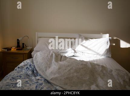 Ungemachtes Bett, beleuchtet von Morgensonne Stockfoto