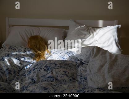 Eine blonde Frau (Schaufensterpuppe), die im Bett schläft und von Morgensonne beleuchtet wird Stockfoto