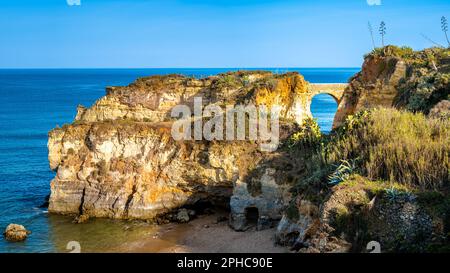 Die historische Ponte Romana de Lagos steht inmitten des goldenen Lichtes und verbindet zwei Klippen vor dem Horizont des Atlantischen Ozeans. Stockfoto