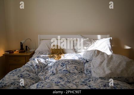 Eine blonde Frau (Schaufensterpuppe), die im Bett schläft und von Morgensonne beleuchtet wird Stockfoto