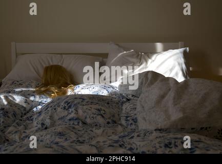 Eine blonde Frau (Schaufensterpuppe), die im Bett schläft und von Morgensonne beleuchtet wird Stockfoto