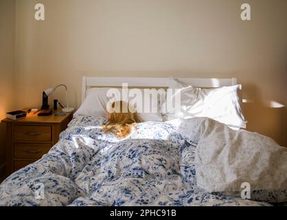 Eine blonde Frau (Schaufensterpuppe), die im Bett schläft und von Morgensonne beleuchtet wird Stockfoto