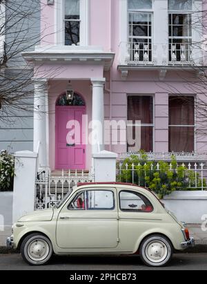 Süßes beigefarbenes Oldtimer Fiat 500 vor einem Haus mit einer pinkfarbenen Tür in einer Wohnstraße in Notting Hill, West London UK. Stockfoto