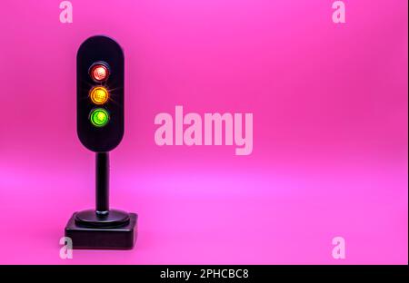 Miniatur-Ampel mit rotem, orangefarbenem und grünem Licht. Studioaufnahme. Rosafarbener leerer Hintergrund. Stockfoto