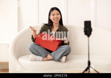 Glückliche asiatische Beeinflusserin mit roter Schuhbox, Streaming Stockfoto