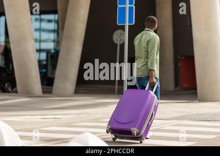 Black Guy Walking Mit Reisekoffer Am Flughafen, Rückansicht Stockfoto