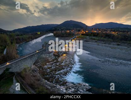 Nächtliche Luftaufnahme der alten mittelalterlichen Brücke, genannt „Ponte del Diavolo“ oder „Ponte Gobbo“, auch „Teufelsbrücke“ über den Fluss Trebbia, Bobbio, Emil Stockfoto