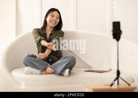 Eine fröhliche, hübsche chinesin, die Videos auf dem Smartphone aufnimmt, Inneneinrichtung Stockfoto