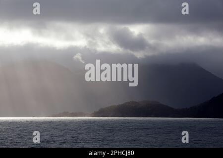 Der Blick am Morgen auf eine bewölkte bergige Küste mit Sonnenlicht im Fiordland-Nationalpark (Neuseeland). Stockfoto