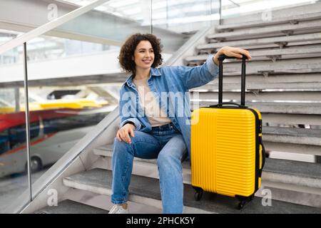 Wunderschöne Junge Frau Mit Gepäck, Die Auf Der Treppe Am Flughafen Sitzt Stockfoto