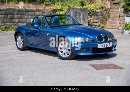 Der zweitürige Sportwagen BMW Z3 parkt an einem sonnigen Tag in einer Sackgasse mit einer Steinmauer und Hütten dahinter Stockfoto