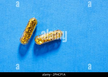 Zwei Pillen gefüllt mit goldenem Glitzer auf blauem Hintergrund. Kreatives Konzept, Drogen, Pillen Stockfoto
