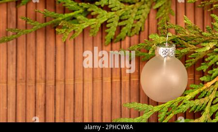 Weihnachtsschmuck aus Milchglas mit grünen Ästen auf hölzernem Hintergrund Stockfoto