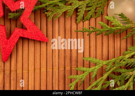 Festlicher roter Stern und mattiertes Ornament mit grünen Ästen auf hölzernem Hintergrund Stockfoto