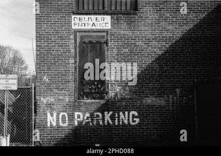 Die Straßenseite eines verwitterten viktorianischen Backsteingebäudes mit „kein Parkplatz“ an der Wand und einem Schild mit der Aufschrift „Liefereingang“ in Stoneham, Massachu Stockfoto