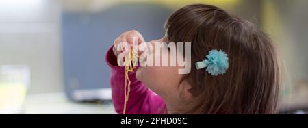 Bild eines liebenswerten brünetten kleinen Mädchens, das Spaghetti mit den Händen isst. Horizontales Banner Stockfoto