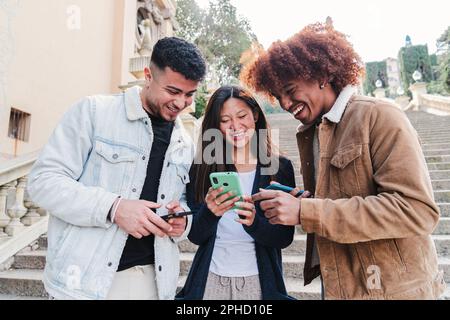 Eine Gruppe multiethnischer Teenager, die lustige Videos in einer Social-Media-App mit einem Mobiltelefon anschauen. Drei junge Freunde teilen Inhalte und haben gemeinsam Spaß mit einem Smartphone. Glückliche Leute mit Telefon. Hochwertiges Foto Stockfoto