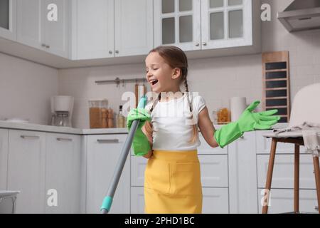 Süßes kleines Mädchen mit Mopp, das beim Putzen zu Hause singt Stockfoto