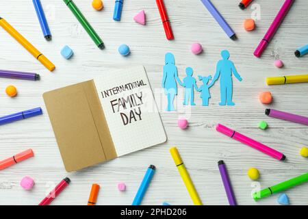 Alles Gute Zum Familientag. Flachliegenkomposition mit Papiereltern und ihren Kindern in der Nähe von Notizbuch auf weißem Holztisch Stockfoto