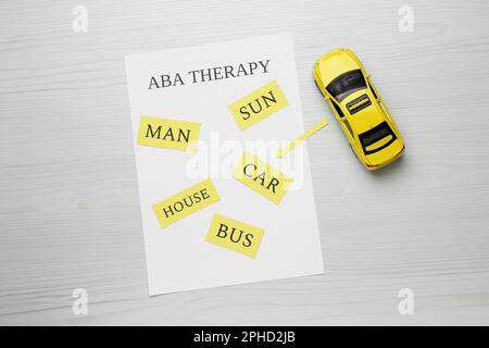 Taxifahrzeugmodell und Papierbogen mit Phrase ABA Therapy auf weißem Holztisch, flach liegend Stockfoto