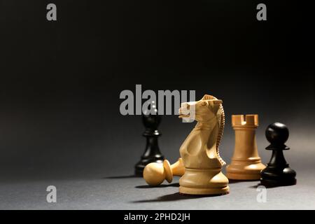 Verschiedene Schachfiguren vor dunklem Hintergrund, konzentriere dich auf den weißen Ritter. Platz für Text Stockfoto