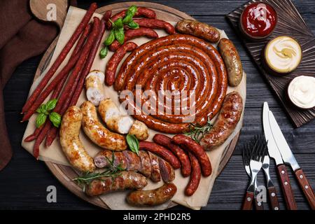 Verschiedene leckere Würstchen mit Kräutern und Soßen auf schwarzem Holztisch, flach liegend. Auswahl an Biersnacks Stockfoto