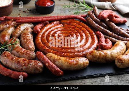 Verschiedene köstliche Würstchen mit Rosmarin und Saucen auf Holztisch, Nahaufnahme. Auswahl an Biersnacks Stockfoto