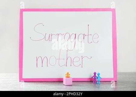 MYKOLAIV, UKRAINE - 04. JANUAR 2022: Tafel mit den Wörtern Surrogate Mother, Cube und Human Figures auf grauem Tisch Stockfoto