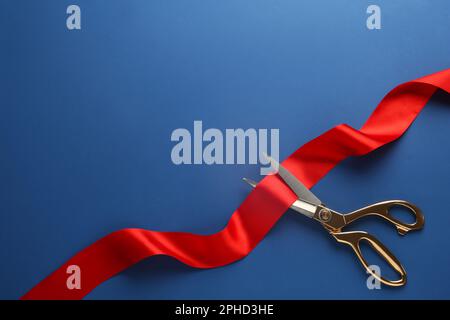 Rotes Band und Schere auf blauem Hintergrund, Draufsicht. Platz für Text Stockfoto