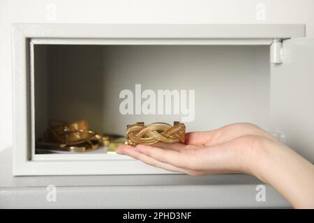 Eine Frau, die ein goldenes Armband aus einem Safe auf dem Tisch nimmt, vor hellem Hintergrund, Nahaufnahme Stockfoto