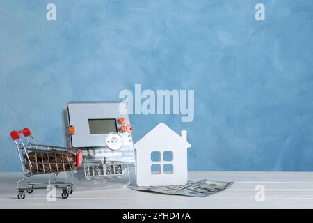 Stromzähler, Hausmodell, kleiner Einkaufswagen mit Münzen und Dollarscheine auf weißem Holztisch. Platz für Text Stockfoto