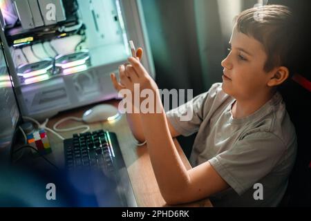 Ein Teenager sitzt zu Hause an einem Tisch und schreibt SMS in einem sozialen Netzwerk oder spielt Videospiele. Stockfoto