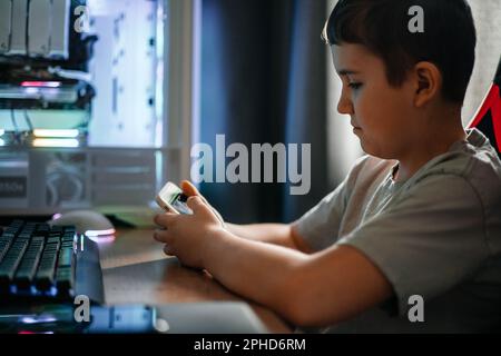 Ein Teenager sitzt zu Hause an einem Tisch und schreibt SMS in einem sozialen Netzwerk oder spielt Videospiele. Stockfoto