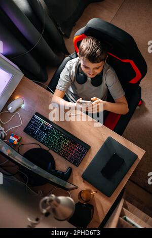 Ein Teenager sitzt zu Hause an einem Tisch und schreibt SMS in einem sozialen Netzwerk oder spielt Videospiele. Stockfoto