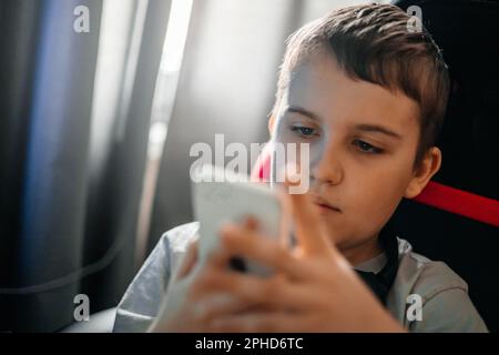 Ein Teenager sitzt zu Hause an einem Tisch und schreibt SMS in einem sozialen Netzwerk oder spielt Videospiele. Stockfoto