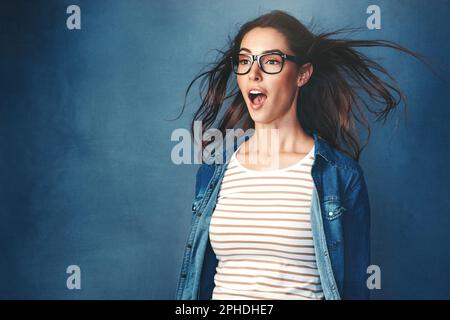 Vergessen Sie nicht, sich selbst zu verblüffen. Studiofoto einer jungen Frau, die vor blauem Hintergrund Luft ins Gesicht geblasen hat. Stockfoto