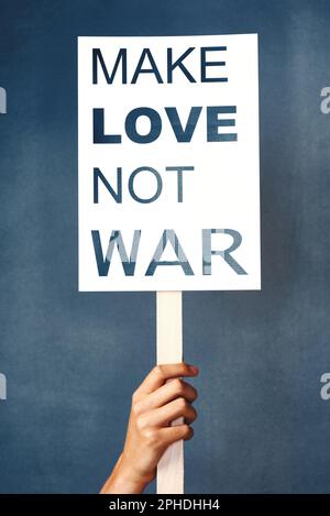 Hass aus der Gesellschaft fernhalten. Studiofoto einer Frau mit einem Schild, auf dem "Make love not war" steht, vor blauem Hintergrund. Stockfoto