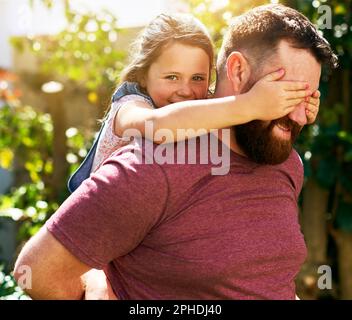 Guck mal, wer dich liebt. Ein bezauberndes kleines Mädchen, das mit ihrem Vater im Garten guckt. Stockfoto