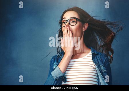 Das ist episch. Studiofoto einer jungen Frau, die vor blauem Hintergrund Luft ins Gesicht geblasen hat. Stockfoto